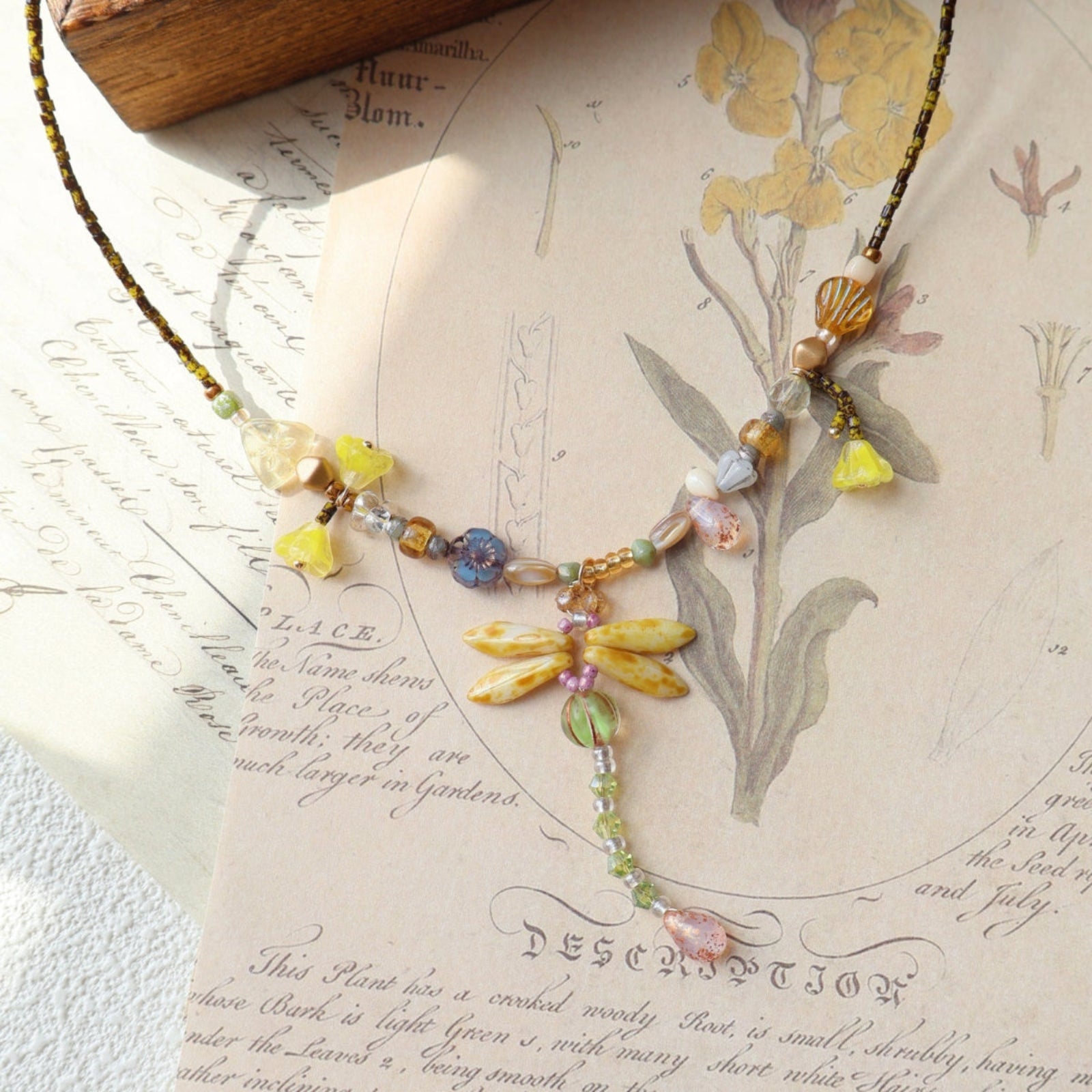 Necklace with floral and dragonfly design on an antique botanical illustration