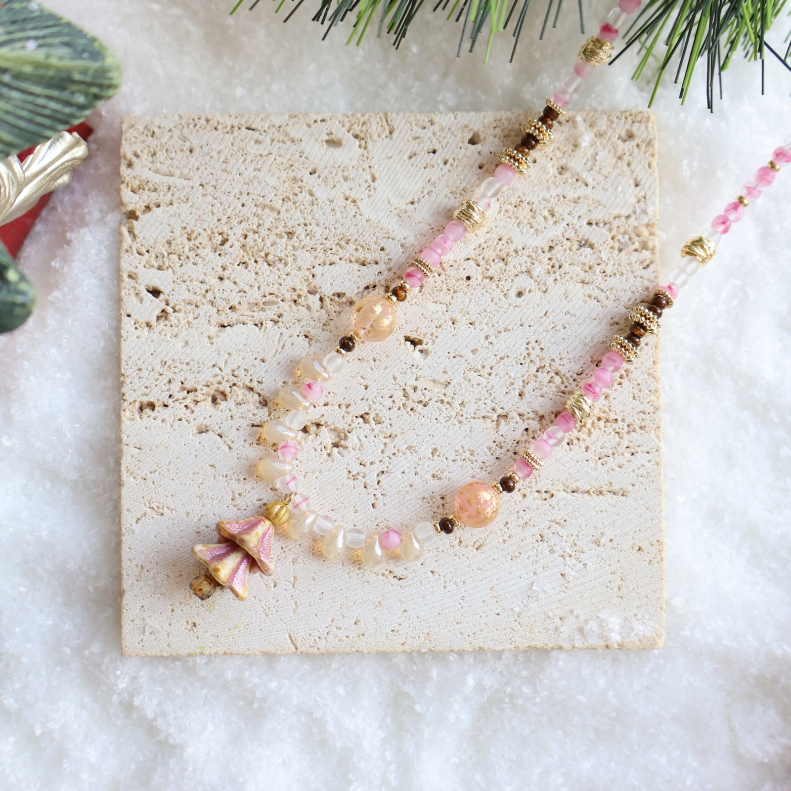 Necklace with pink and gold beads on a textured stone surface with a snowy background