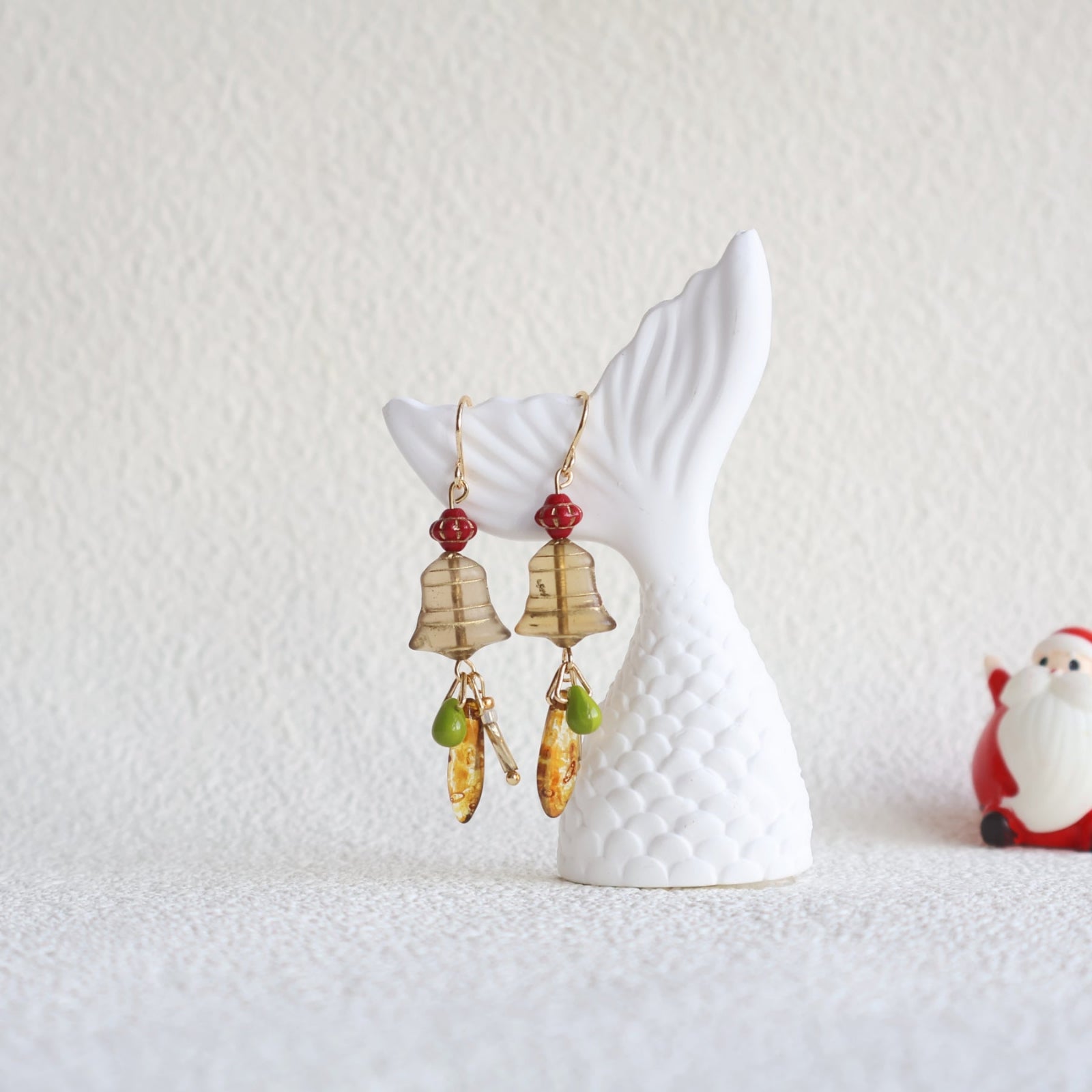 Decorative earrings on a white ceramic stand with a Santa Claus figurine in the background.