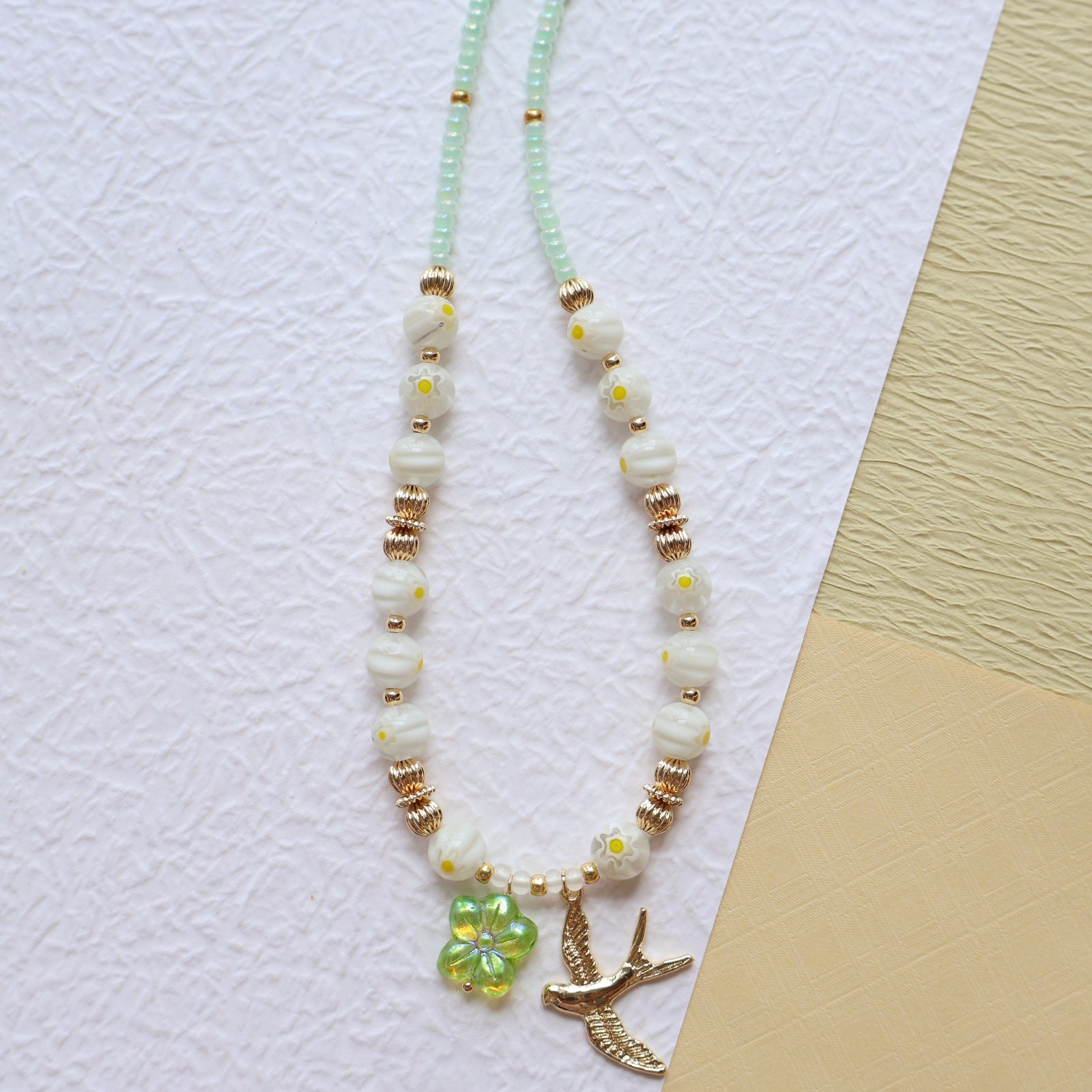 Beaded necklace with floral and bird charms on a textured surface