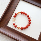 Beaded bracelet with red beads and gold accents on a white surface, framed by a wooden border.