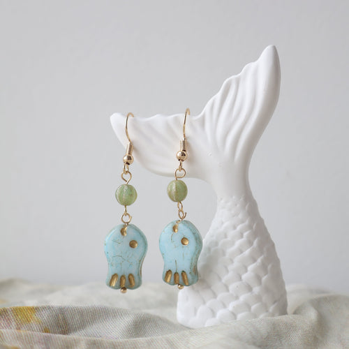Turquoise and gold earrings on a white ceramic stand with a neutral background