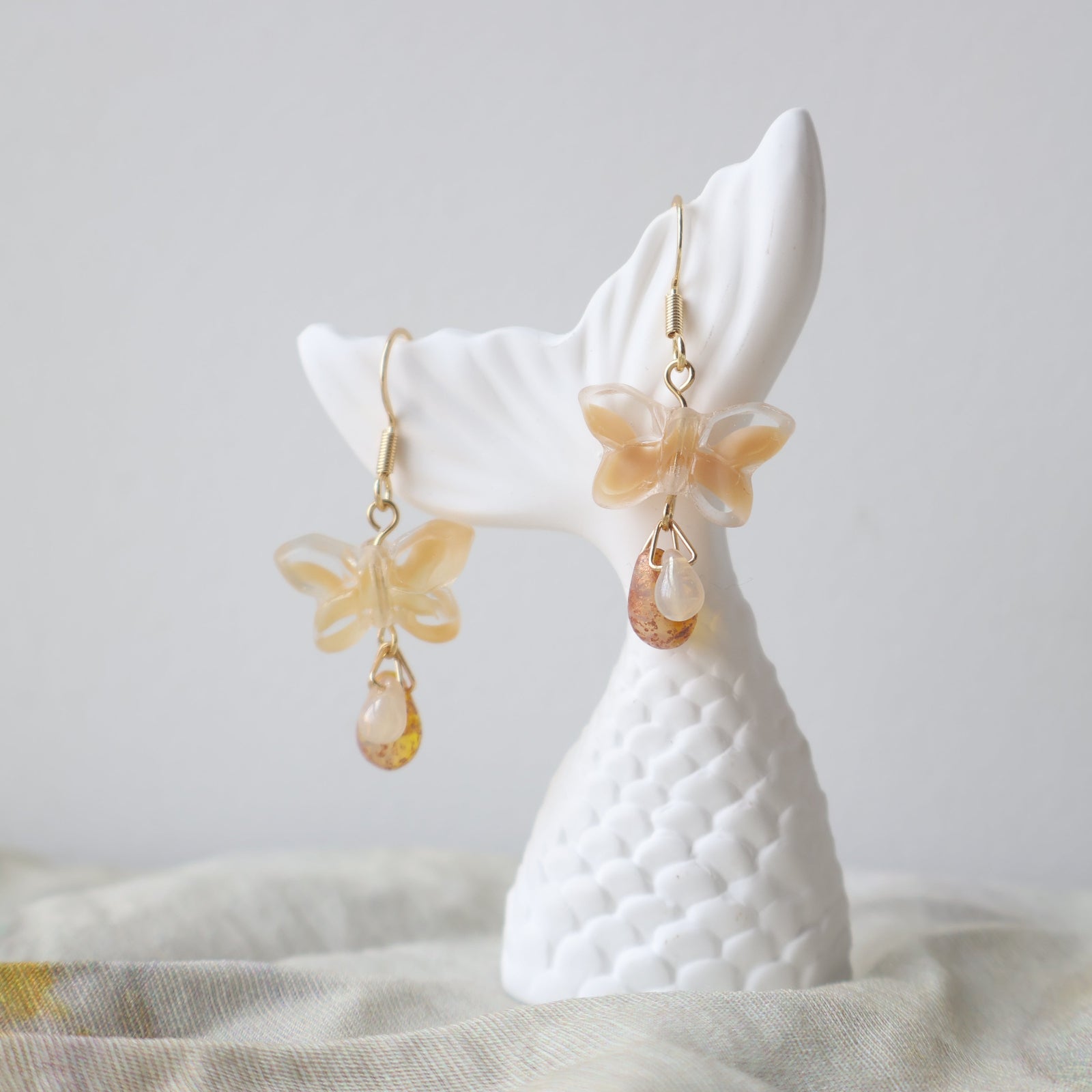 Butterfly-shaped earrings on a white cat-shaped stand against a neutral background