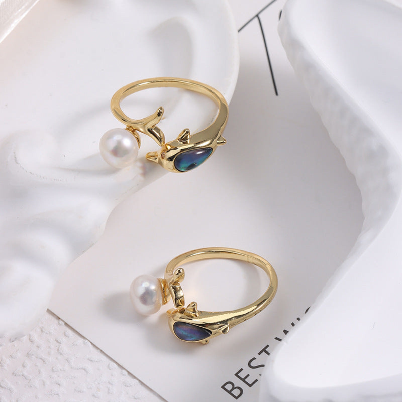 Two gold rings with pearls and gemstones on a white surface