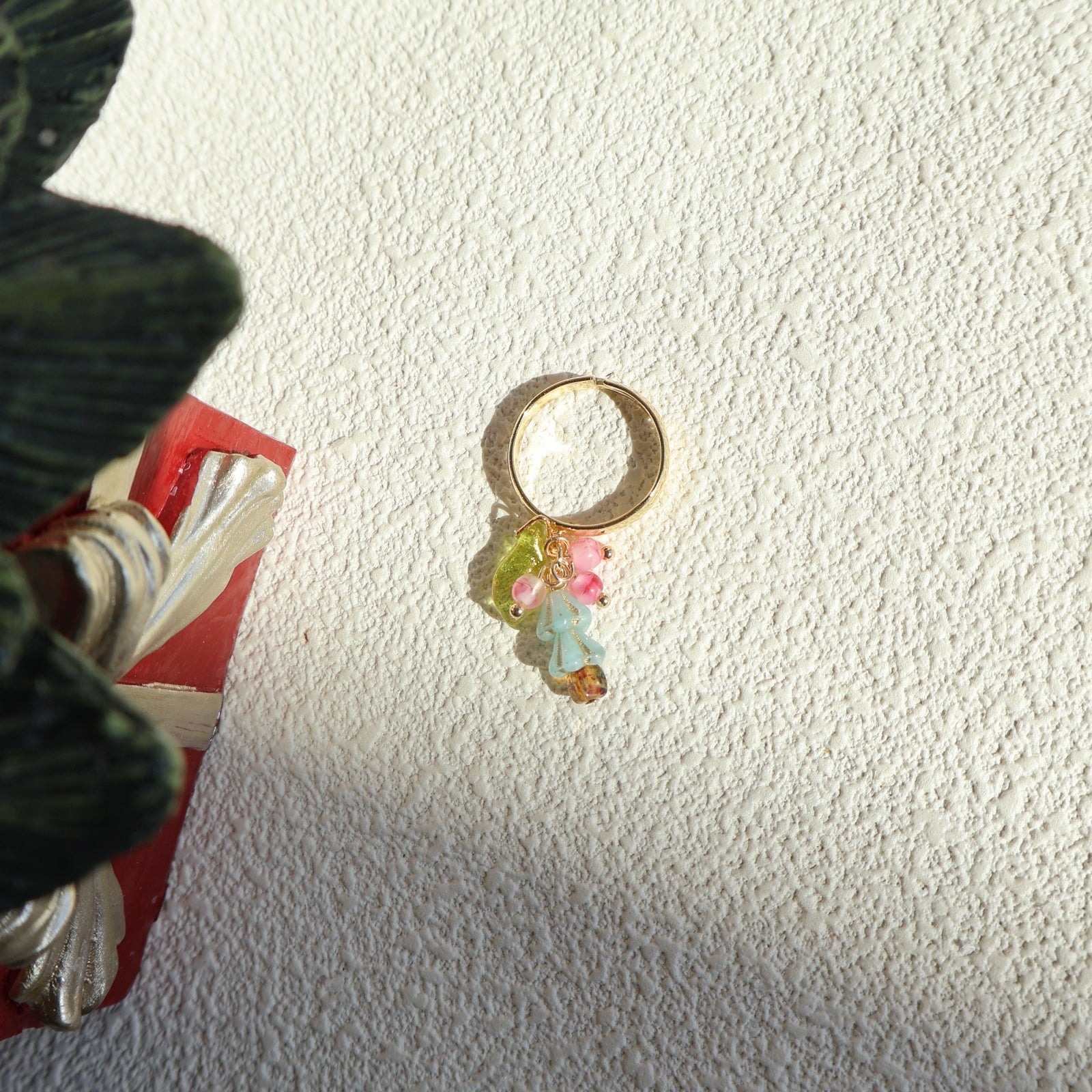 Gold ring with colorful beads on a textured white surface