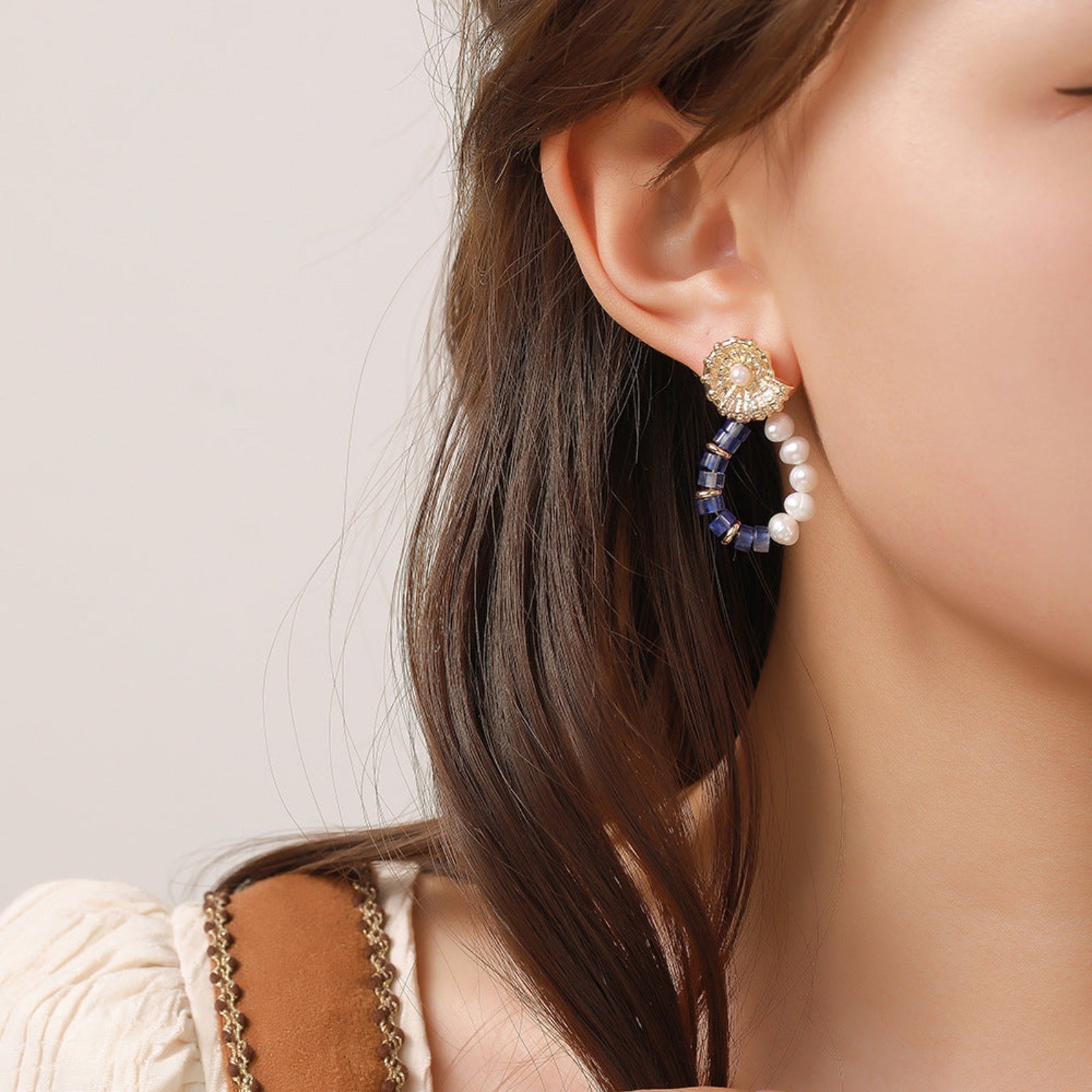 Close-up of a woman wearing a pair of earrings with a neutral background