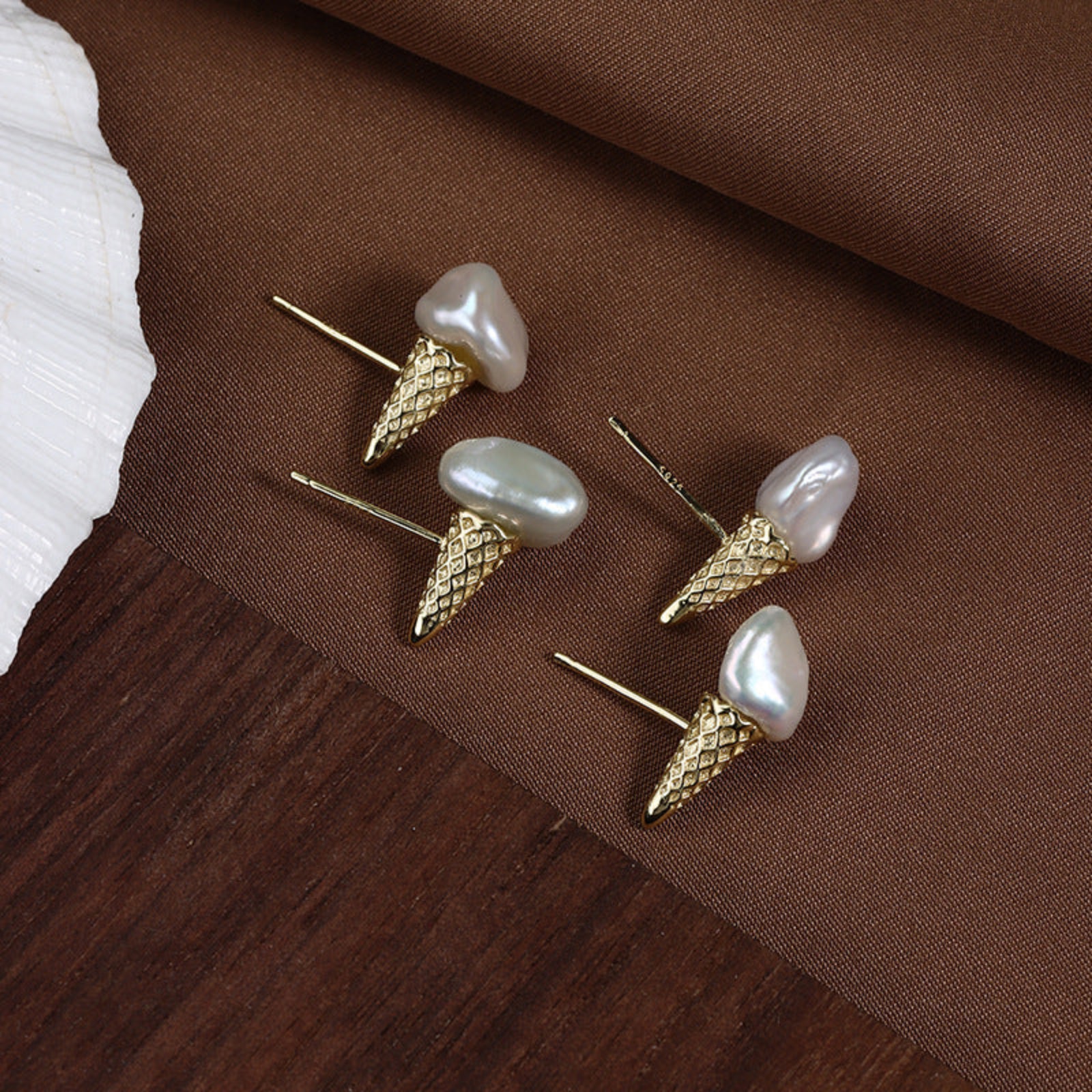 Gold and pearl earrings on a brown fabric background