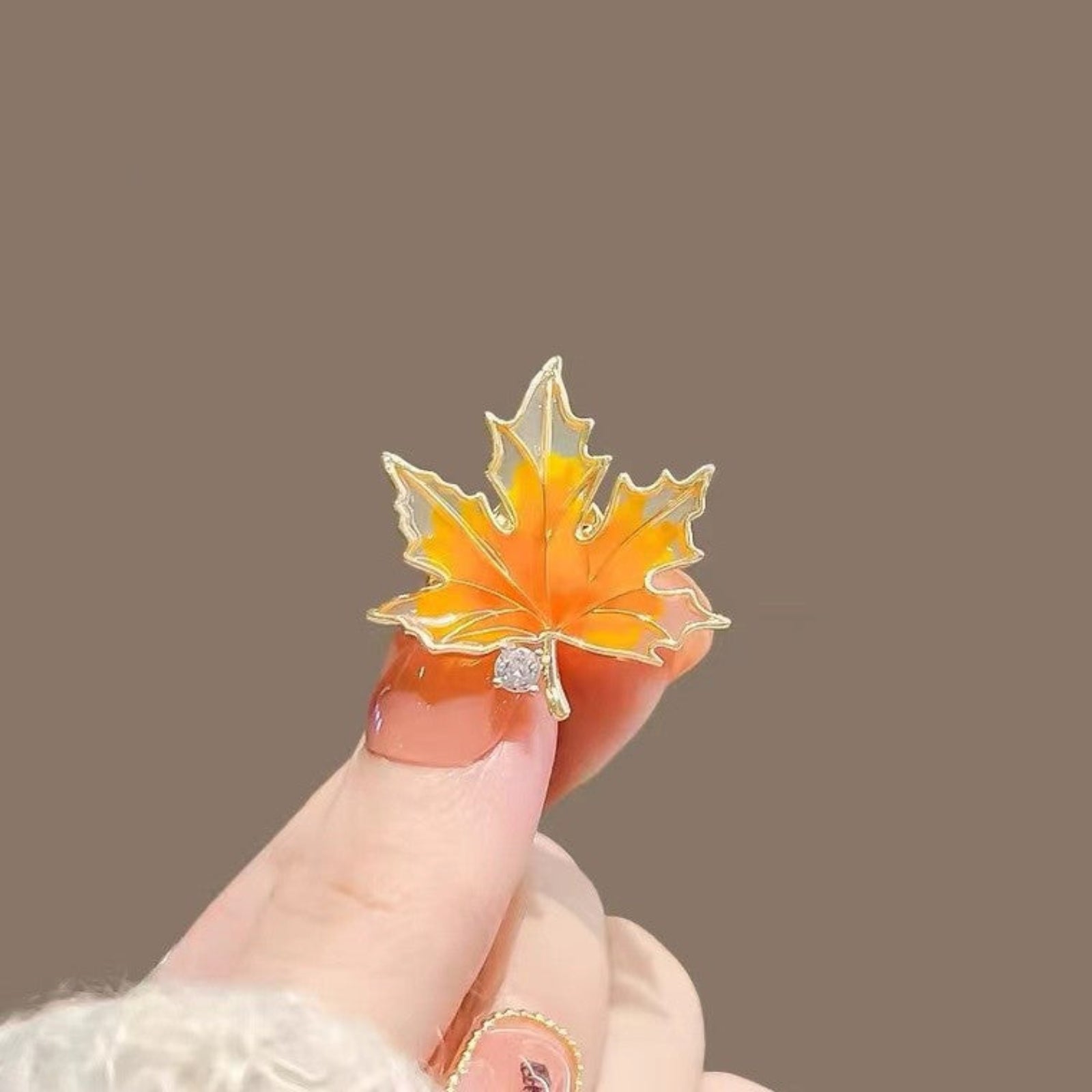 Gold and orange leaf-shaped brooch held by a finger against a brown background