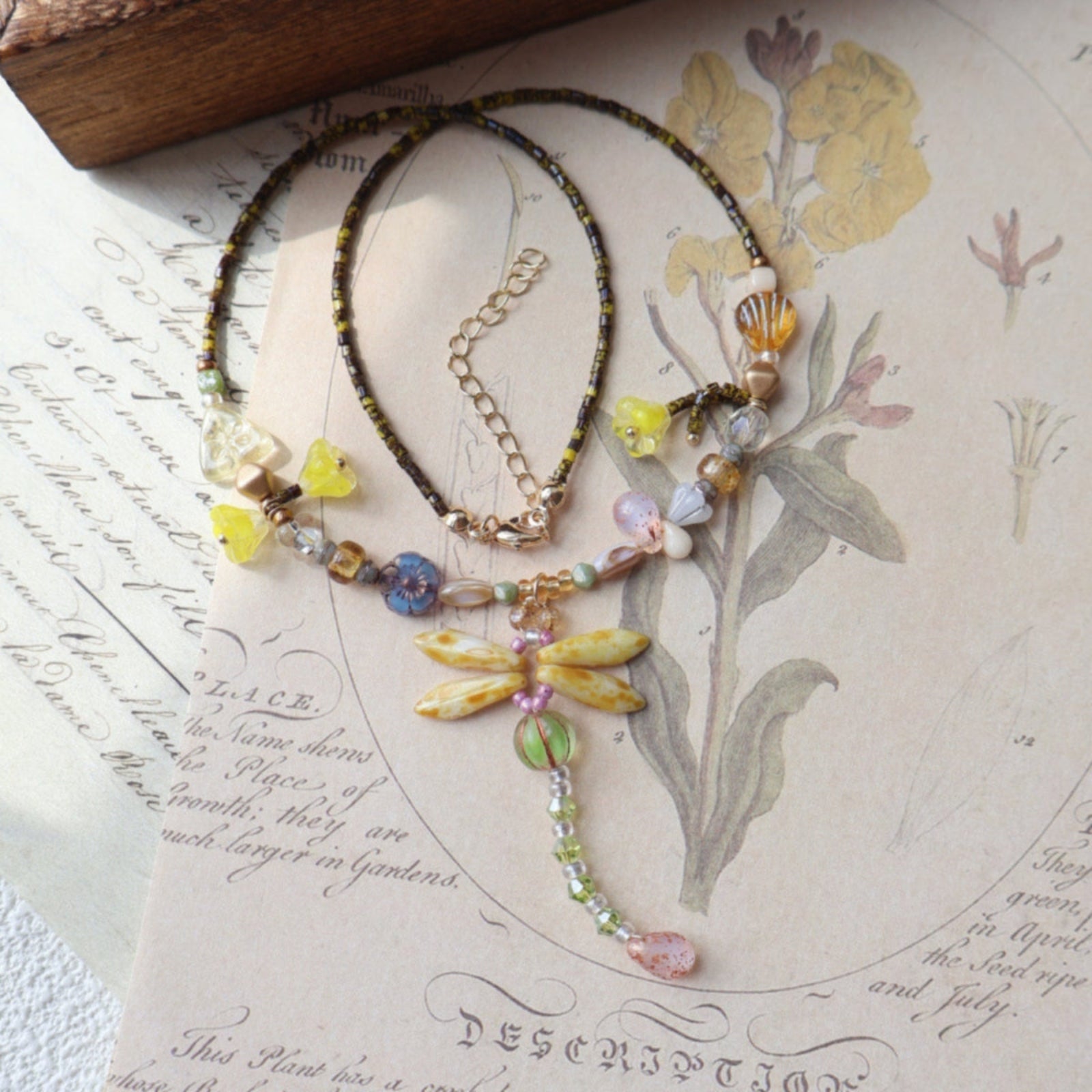 Necklace with dragonfly charm on an old document with floral illustrations