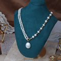 Pearl necklace with a pendant on a teal mannequin bust.
