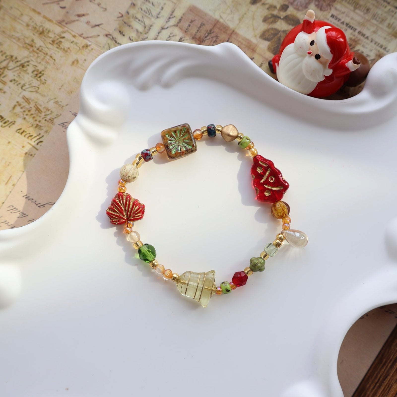 Colorful beaded bracelet on a white dish with a decorative Santa Claus figure in the background.