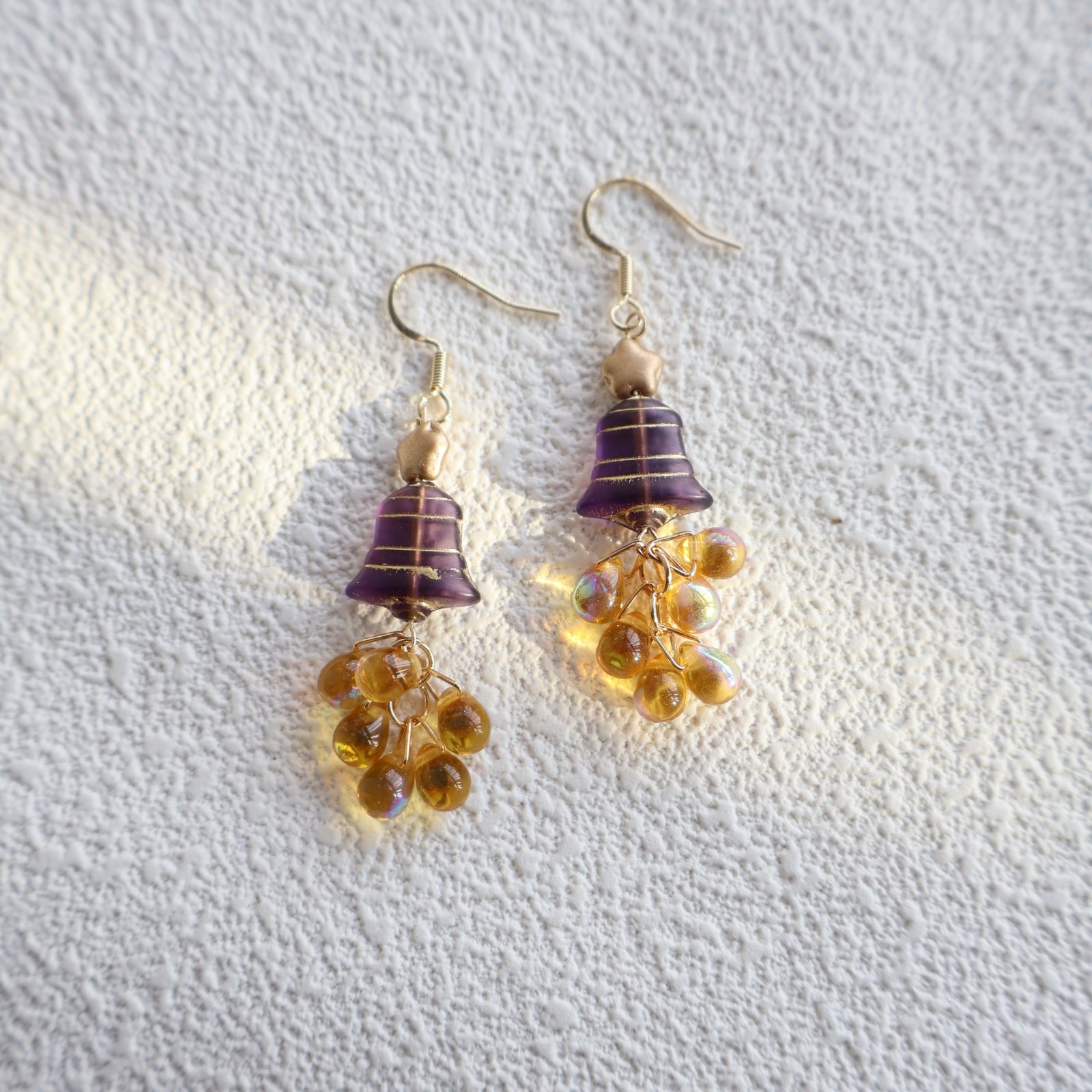 Pair of earrings with purple and gold accents on a textured white background