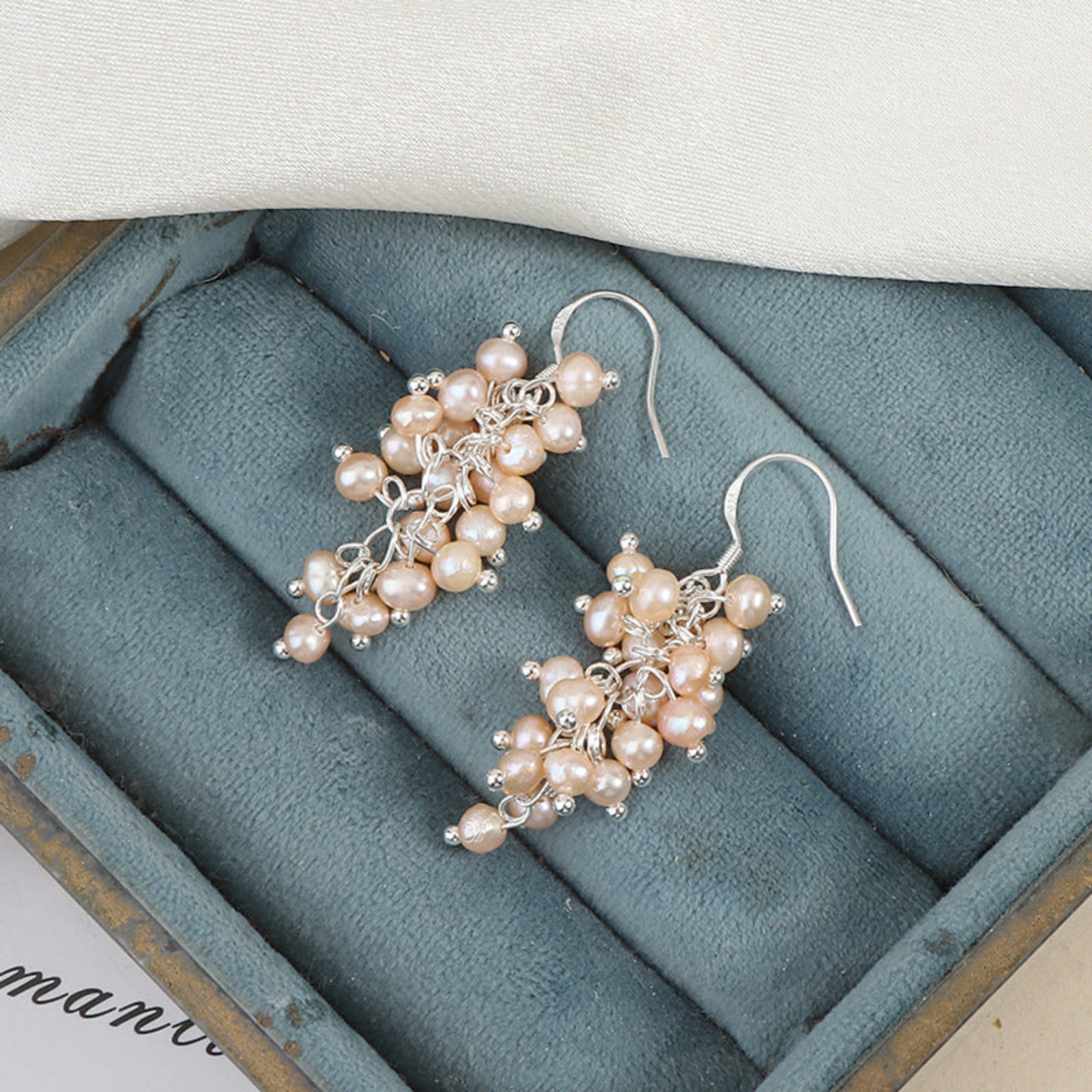 Pair of pearl earrings on a textured blue jewelry box