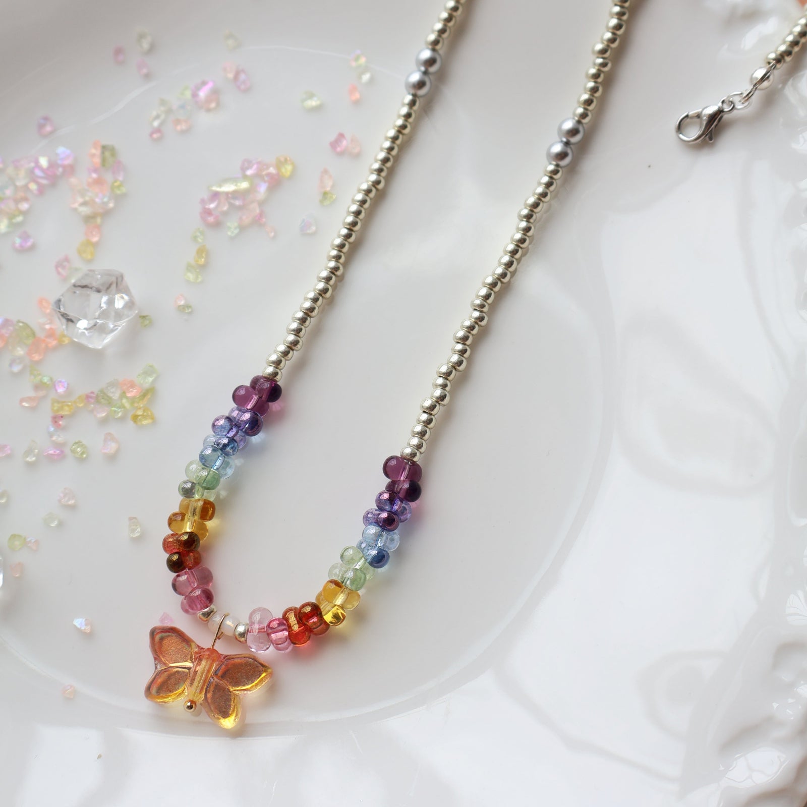 Necklace with colorful beads and a butterfly charm on a white surface with glitter.