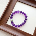Purple beaded bracelet on a white surface inside a wooden frame