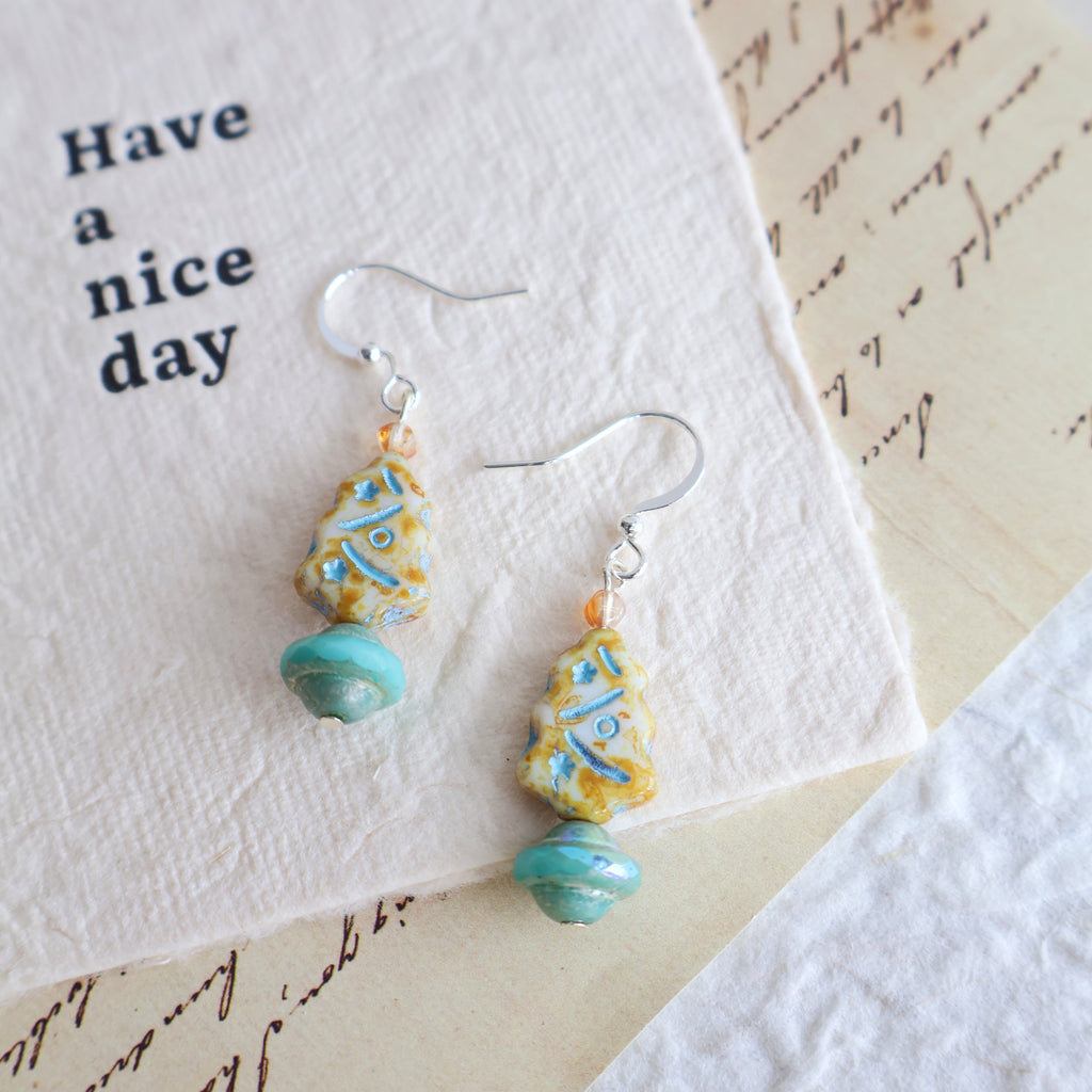 Pair of earrings with turquoise and yellow beads on a card with 'Have a nice day' text.