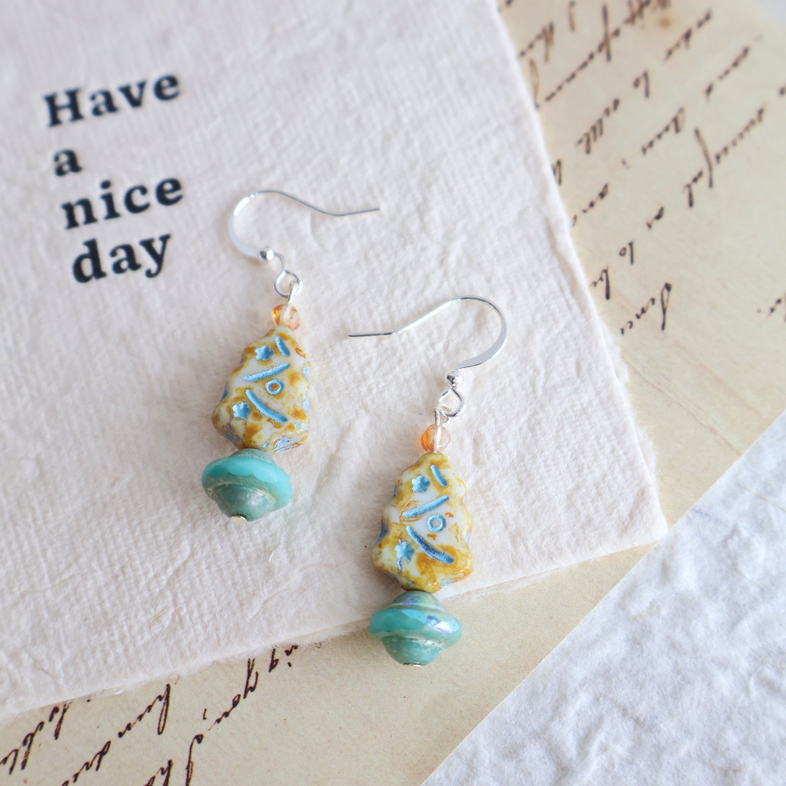 Pair of earrings with turquoise and yellow beads on a card with 'Have a nice day' text.
