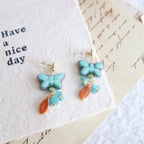 Butterfly-shaped earrings with turquoise stones and gold accents on a textured paper background.