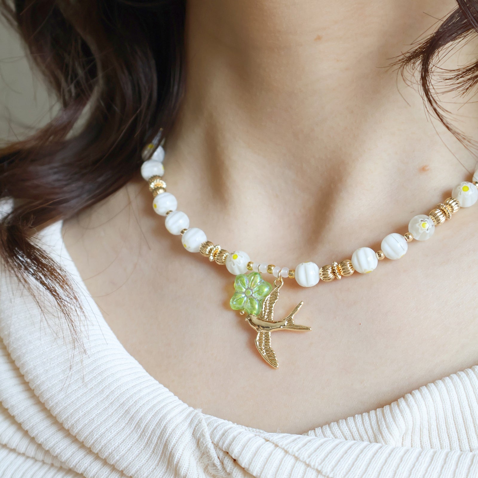 Necklace with white beads and a gold bird charm worn by a person