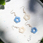 Flower-shaped earrings on a metallic surface with green leaves in the background