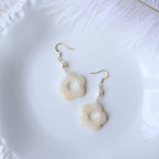 Pair of floral earrings with pearl-like beads on a white textured surface