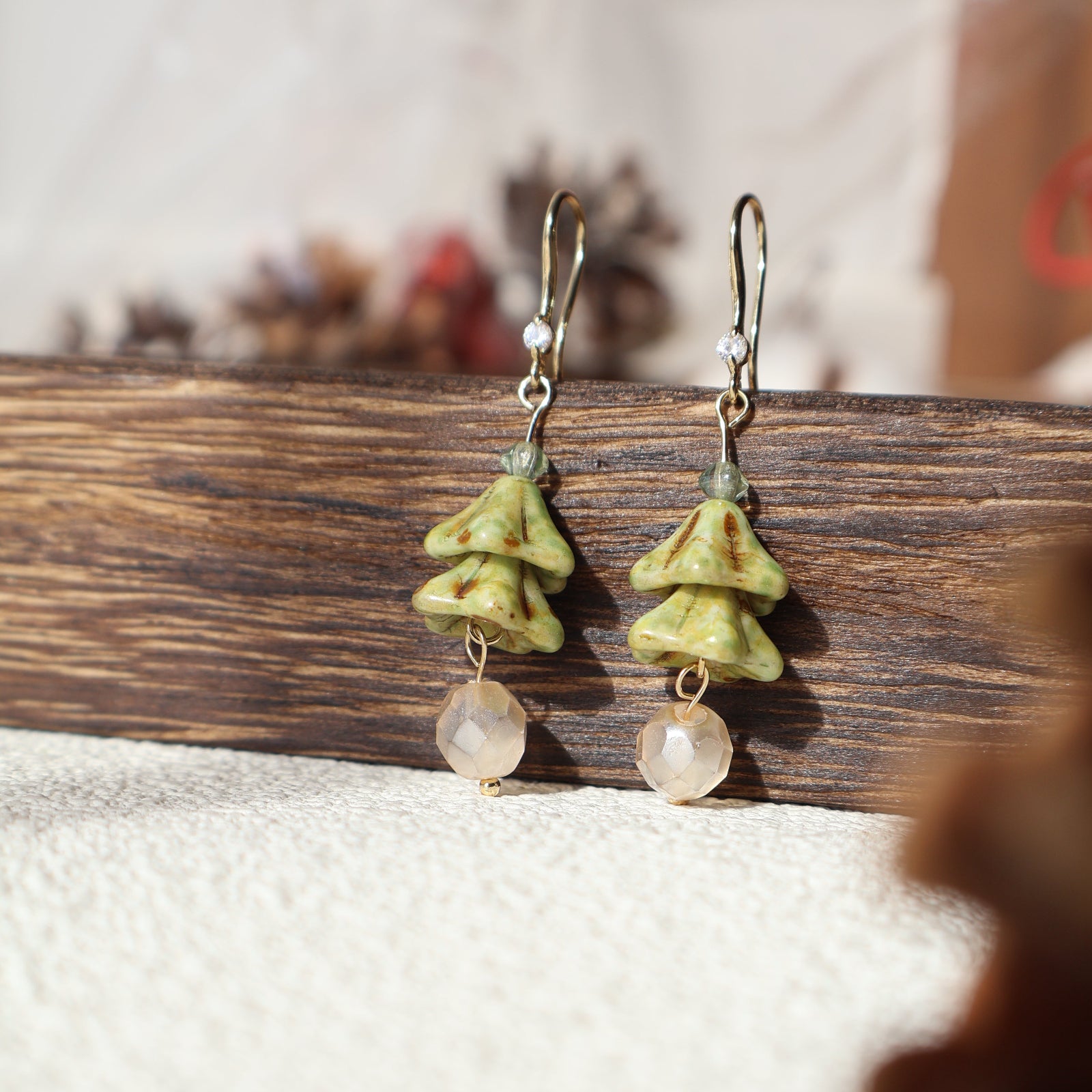 Pair of earrings with green stone-like beads on a wooden stick against a neutral background