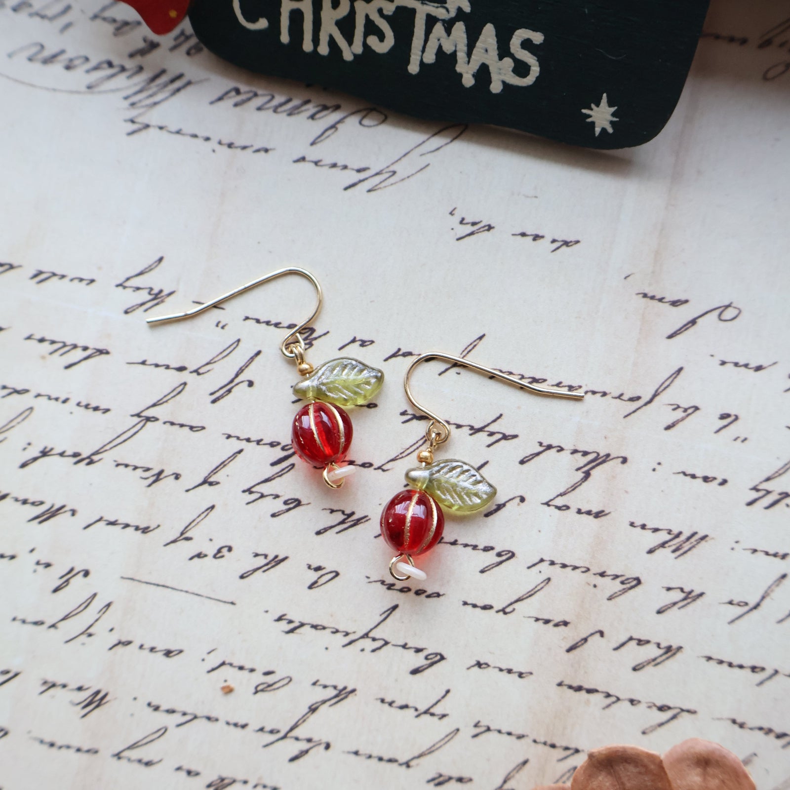 Pair of red and gold earrings on a textured surface with 'Merry Christmas' card.