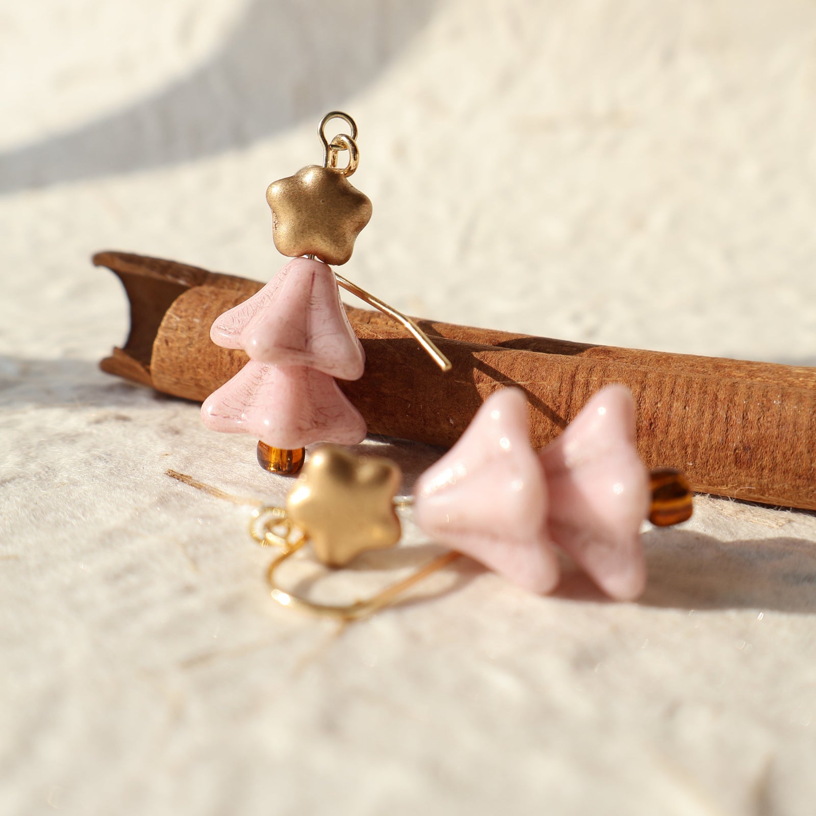 Pair of pink and gold earrings on a wooden stand against a neutral background