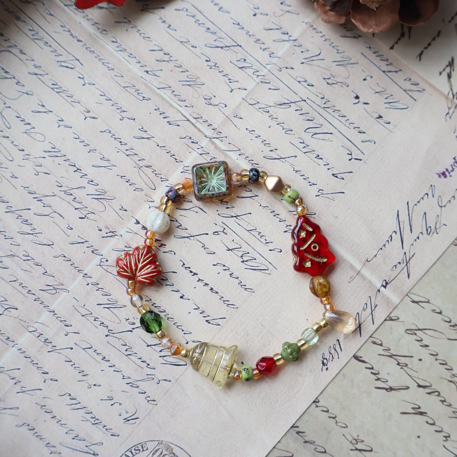 Colorful beaded bracelet on an old letter with a pine cone and Christmas card in the background