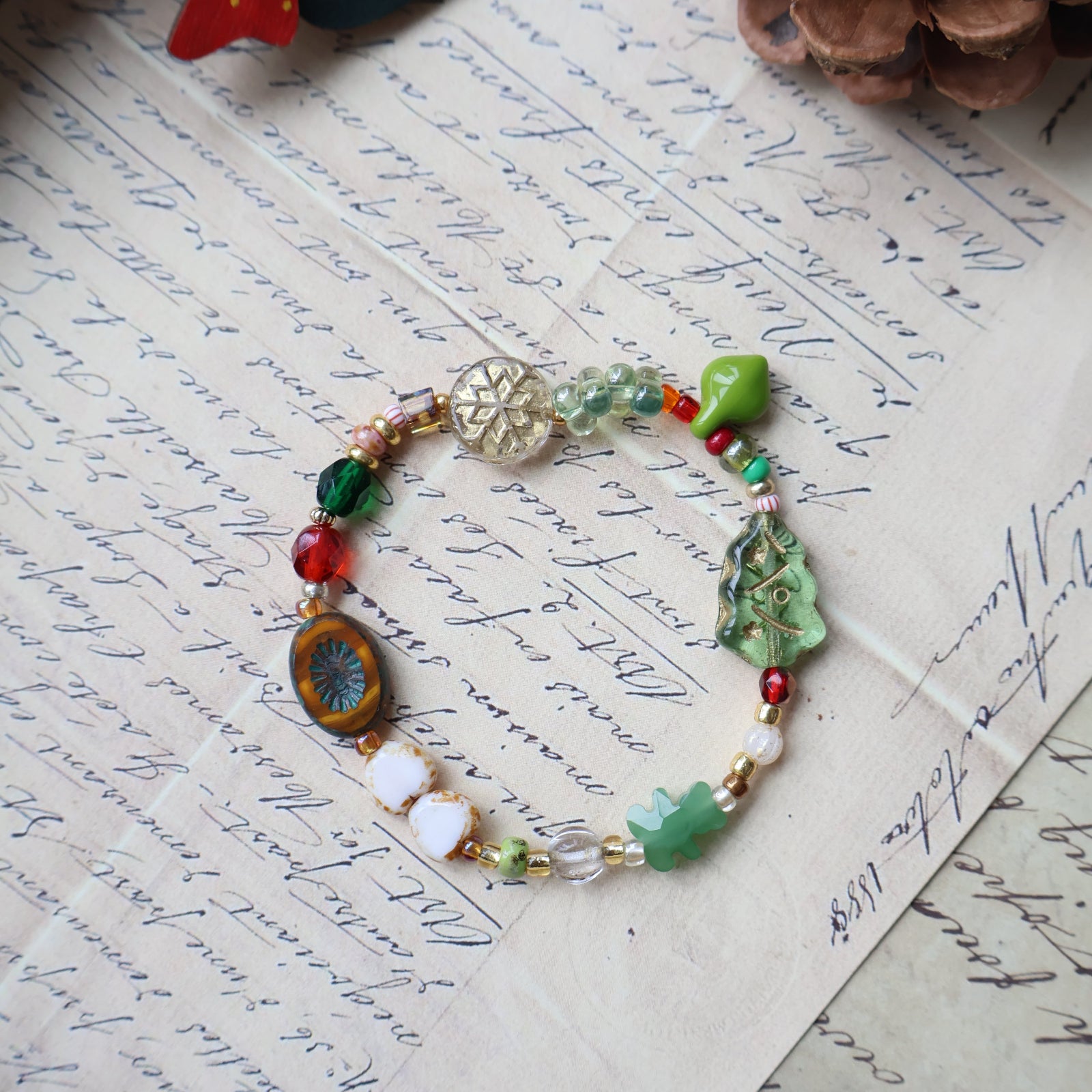 Colorful beaded bracelet on an old letter with a pine cone and Christmas decoration.