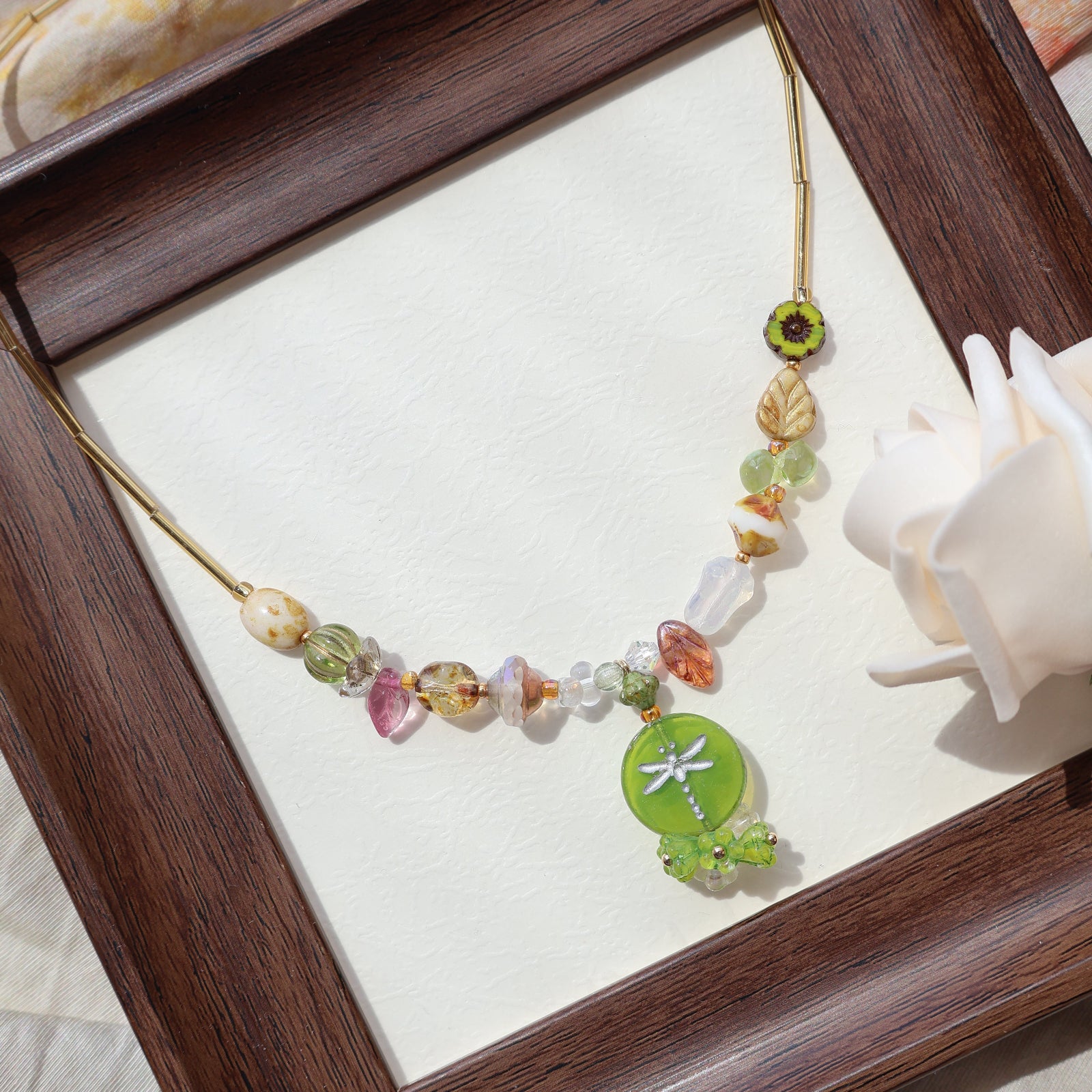 Necklace with colorful beads and a green pendant on a wooden frame.