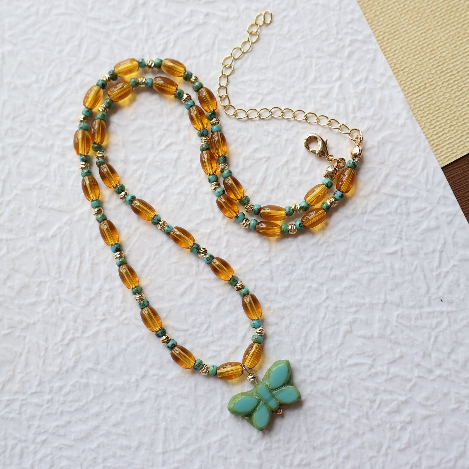 Beaded necklace with a butterfly pendant on a textured white surface