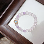 Bracelet with pink beads and gold clasp on a white card inside a wooden frame