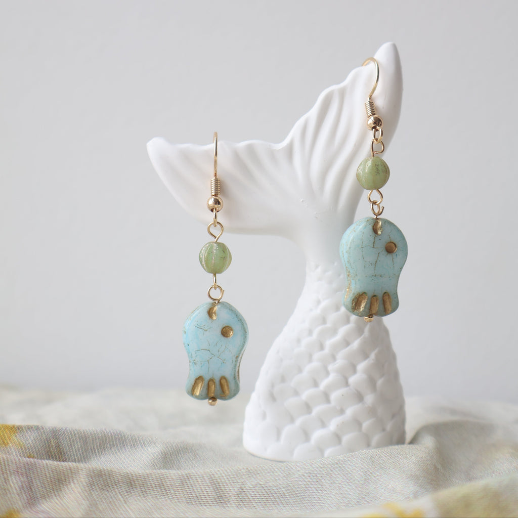 Turquoise and gold earrings on a white ceramic stand with a neutral background