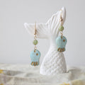Turquoise and gold earrings on a white ceramic stand with a neutral background