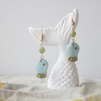 Turquoise and gold earrings on a white ceramic stand with a neutral background