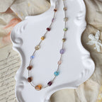 Multicolored beaded necklace on a white shell-shaped dish with a textured fabric background
