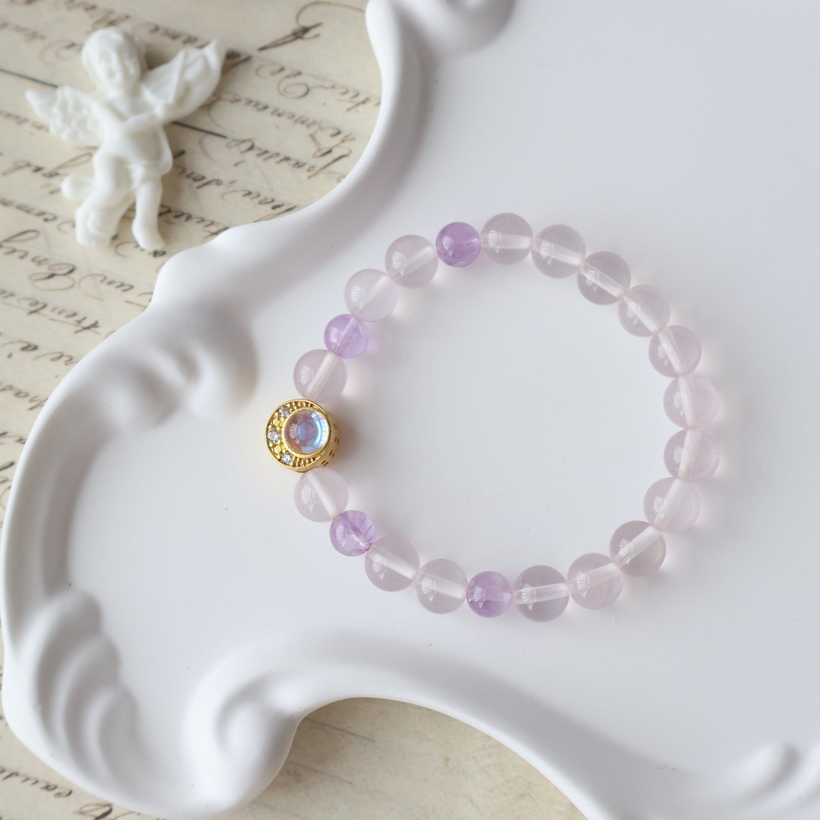 Pink beaded bracelet with a gold clasp on a white dish with a butterfly and text in the background