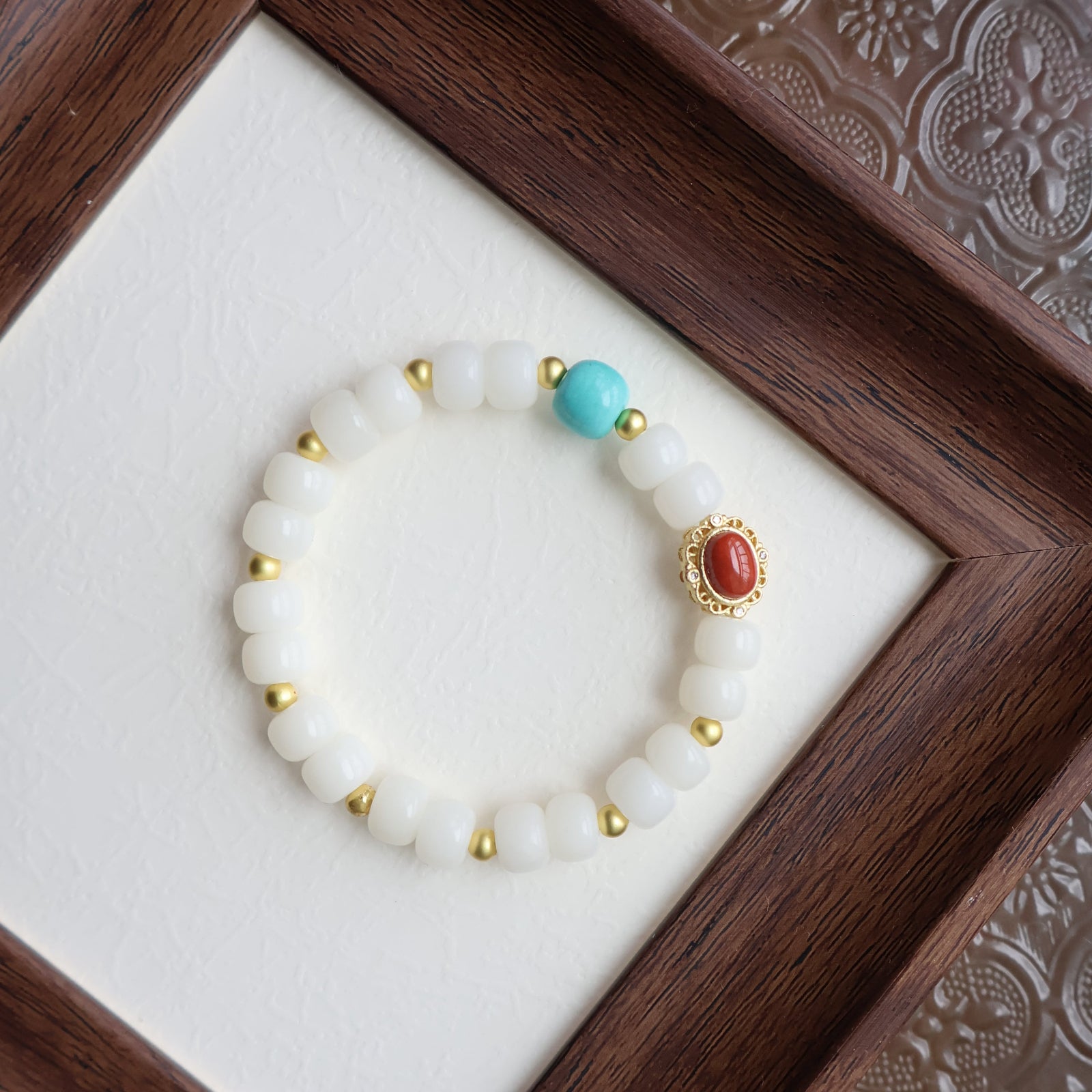 Bracelet with white beads, gold accents, and a red and turquoise bead in a wooden box.