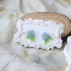 Pair of earrings with floral design on a decorative white stand against a soft fabric background