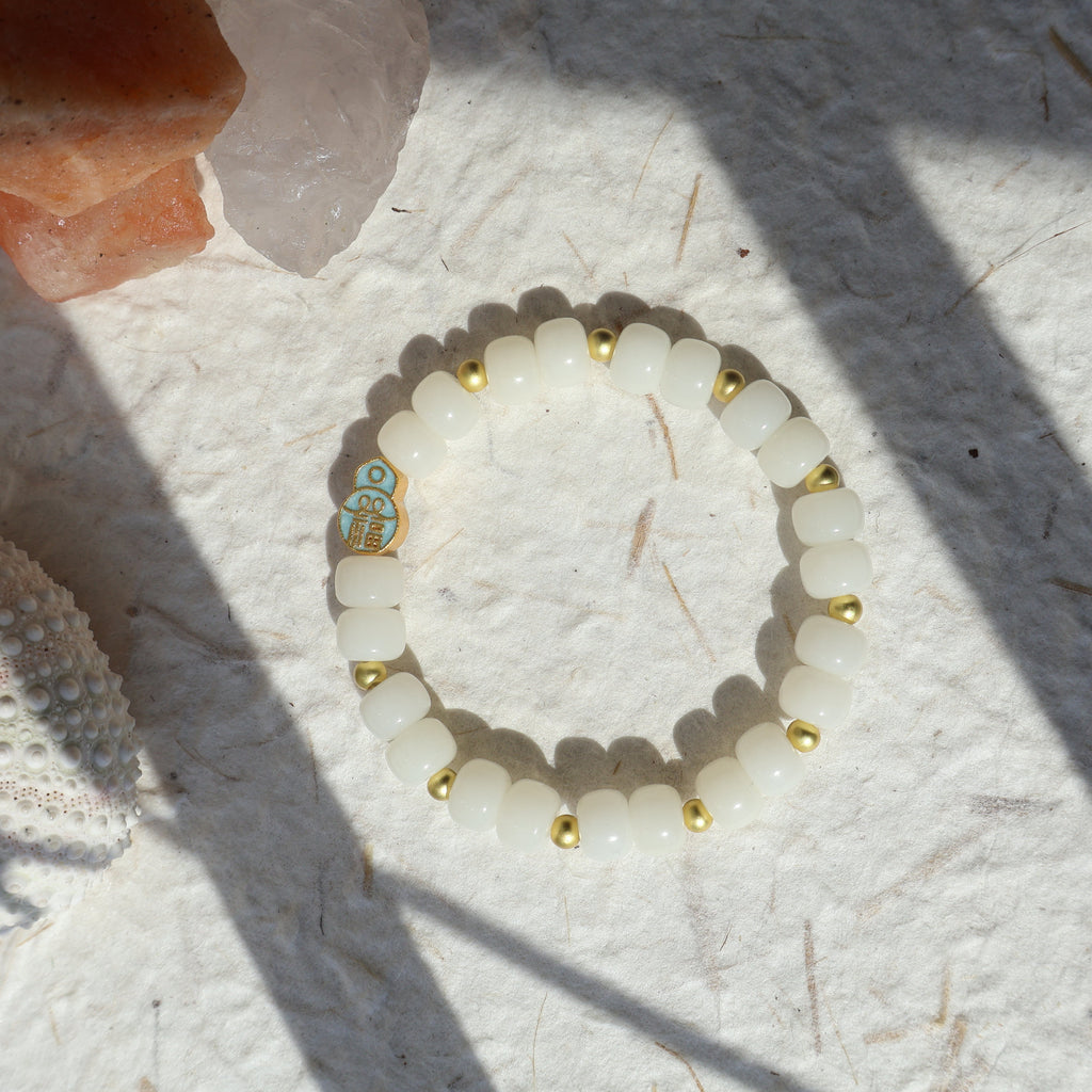 White beaded bracelet with gold accents on a textured white surface with crystals.
