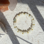 White beaded bracelet with gold accents on a textured white surface with crystals.