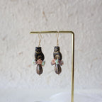 Pair of gold earrings with black and multicolored beads on a light gray background
