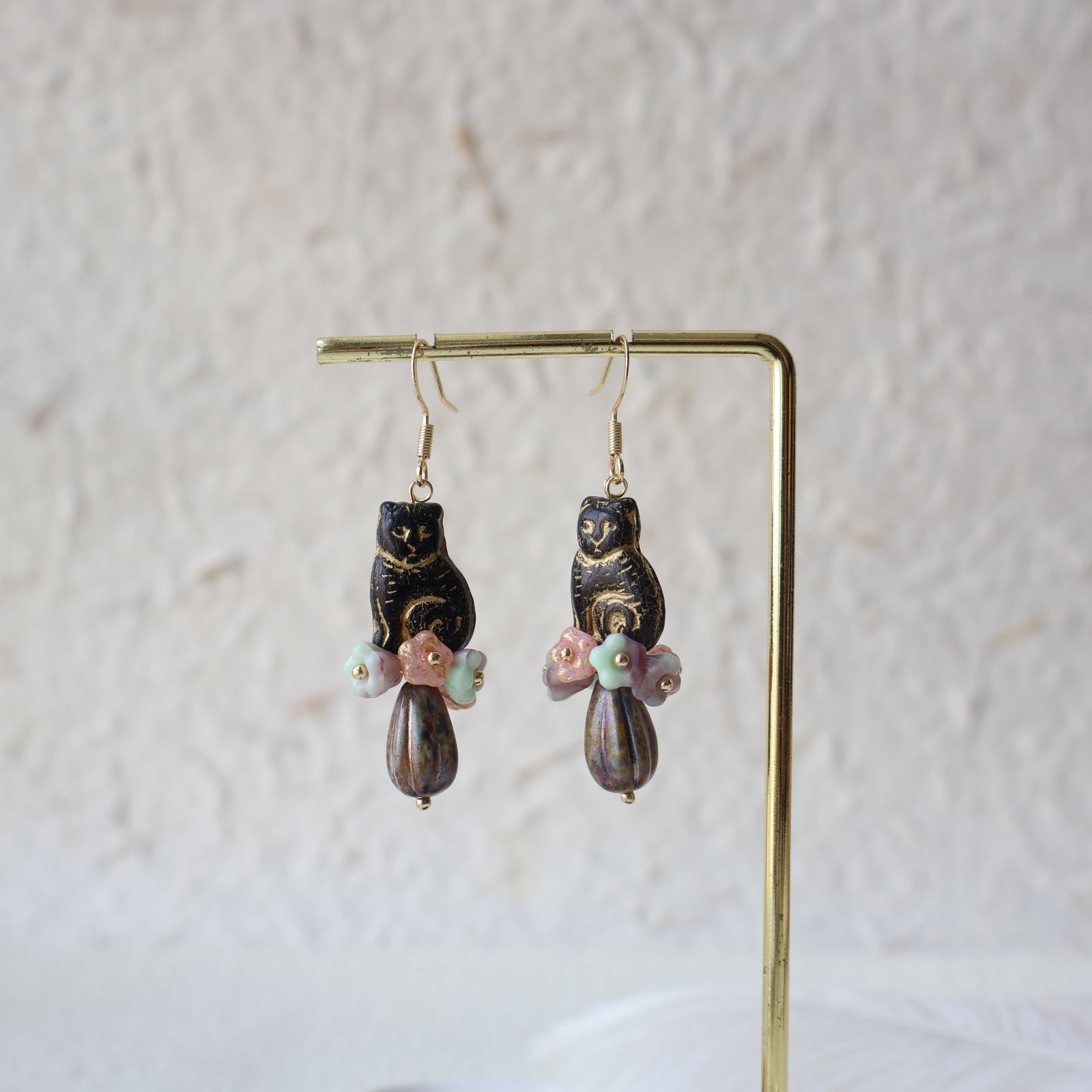 Pair of gold earrings with black and multicolored beads on a light gray background
