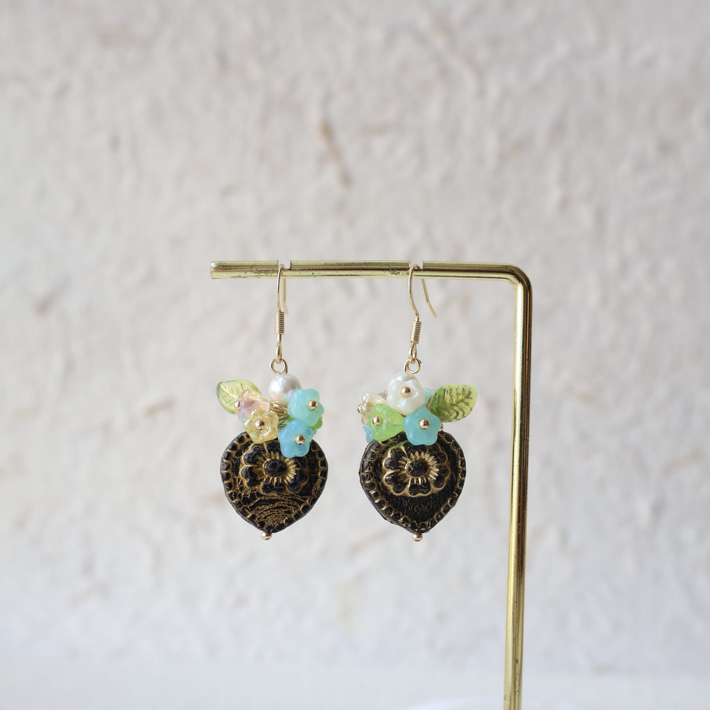 Pair of decorative earrings on a gold stand against a light background