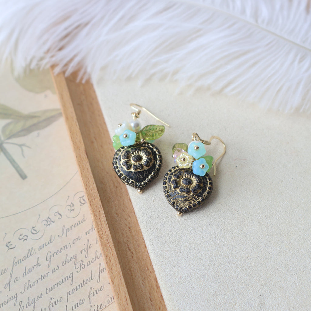 Pair of decorative earrings on a textured surface with a feather and paper in the background