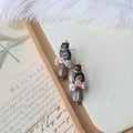 Pair of decorative earrings on a wooden stand with a feather and paper background