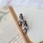 Pair of decorative earrings on a wooden stand with a feather and paper background
