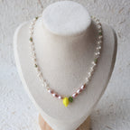 Pearl necklace with a yellow flower pendant on a white stand.
