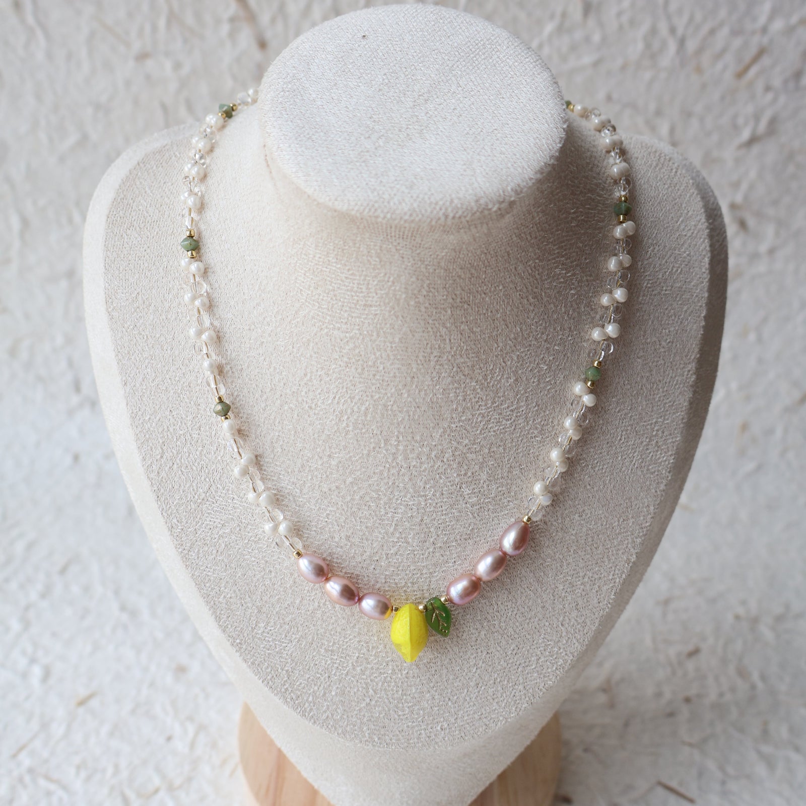Pearl necklace with a yellow flower pendant on a white stand.